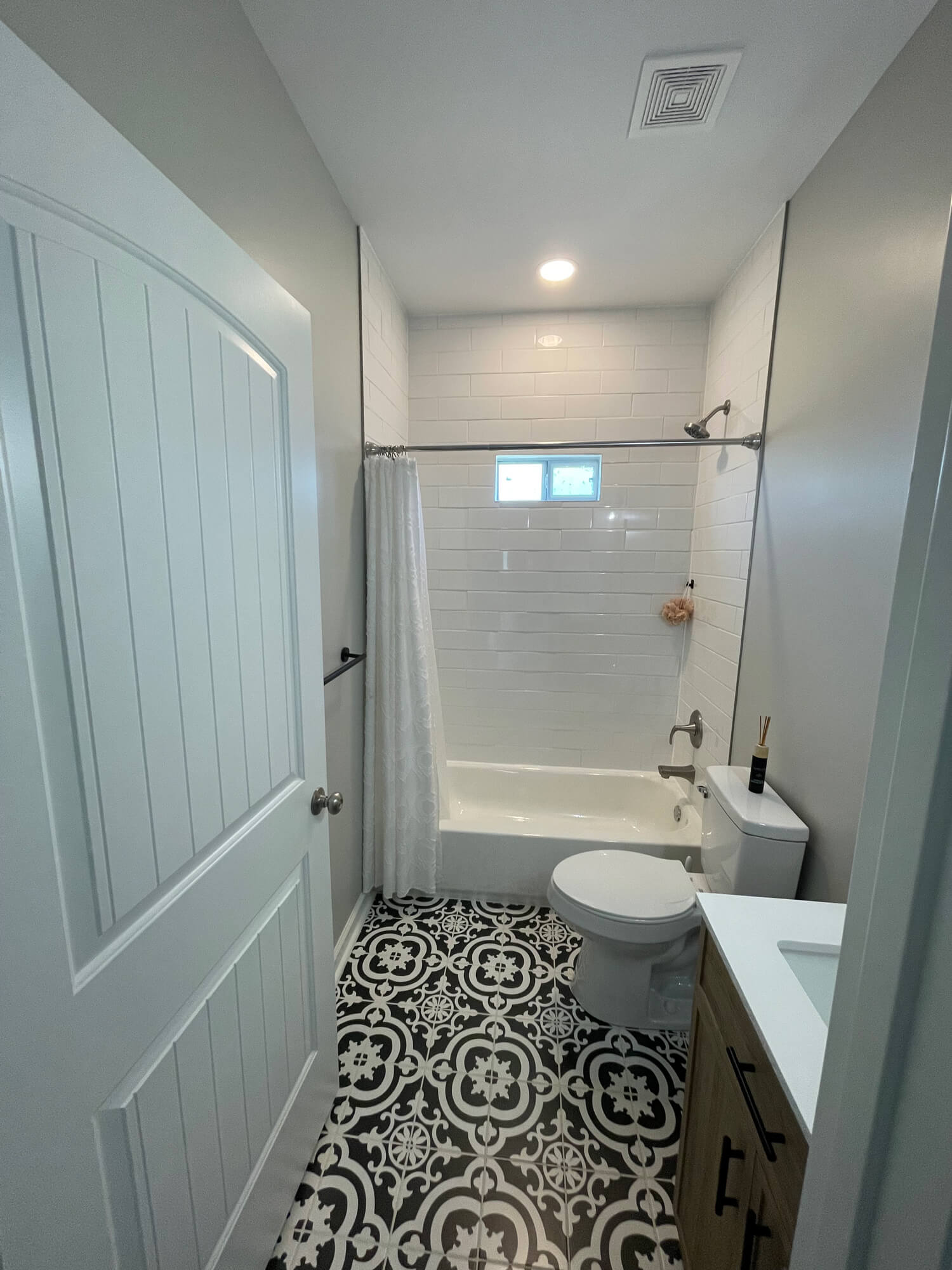 Texas Pro Painters: Modern bathroom featuring a white subway tiled shower, stylish black and white patterned floor tiles, light grey walls, and a new vanity, perfect for interior home renovations.