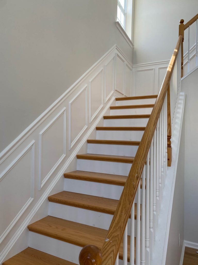 Texas Pro Painters: Elegant residential staircase featuring newly painted white risers and paneling, polished natural wood treads and handrail, and light beige walls, showcasing fine finish carpentry and interior painting.