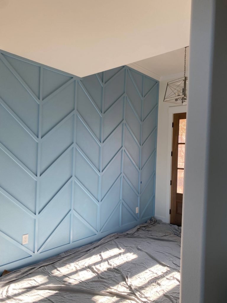 Texas Pro Painters: Interior room with a freshly painted light blue accent wall featuring a decorative chevron wood trim design and a drop cloth covering the floor, highlighting intricate interior painting.
