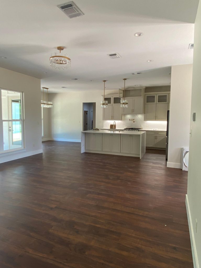 Texas Pro Painters: Newly installed high-end kitchen featuring light beige cabinets, a waterfall island with marble-look countertops, dark wood floors, and elegant gold light fixtures, perfect for cabinet painting and refinishing.