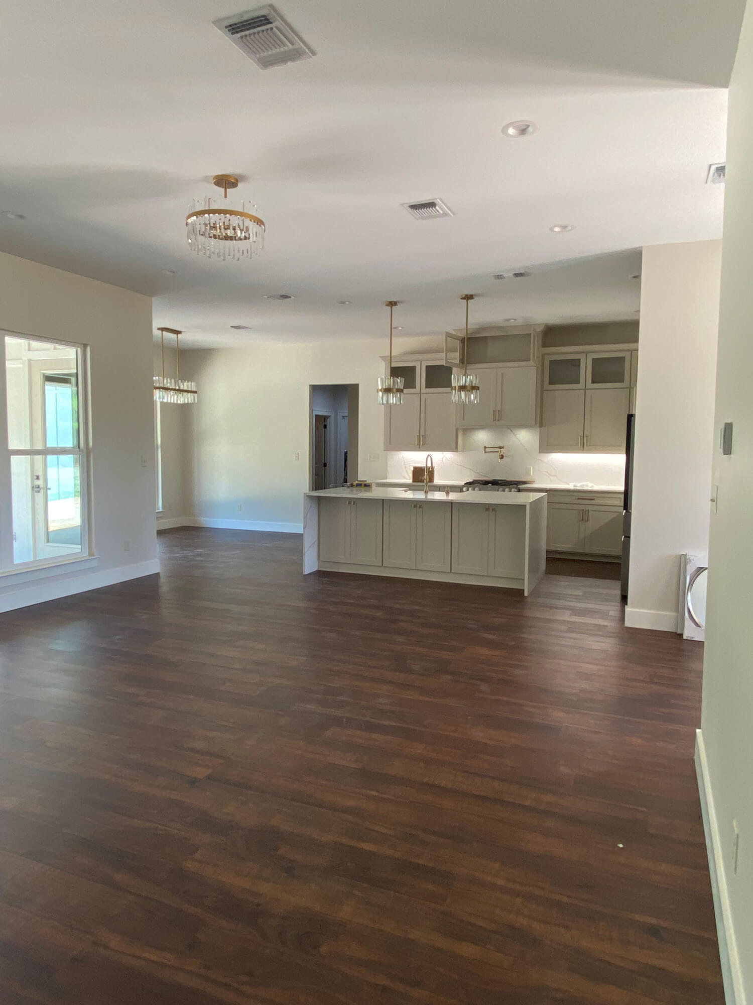 Texas Pro Painters: Newly installed high-end kitchen featuring light beige cabinets, a waterfall island with marble-look countertops, dark wood floors, and elegant gold light fixtures, perfect for cabinet painting and refinishing.