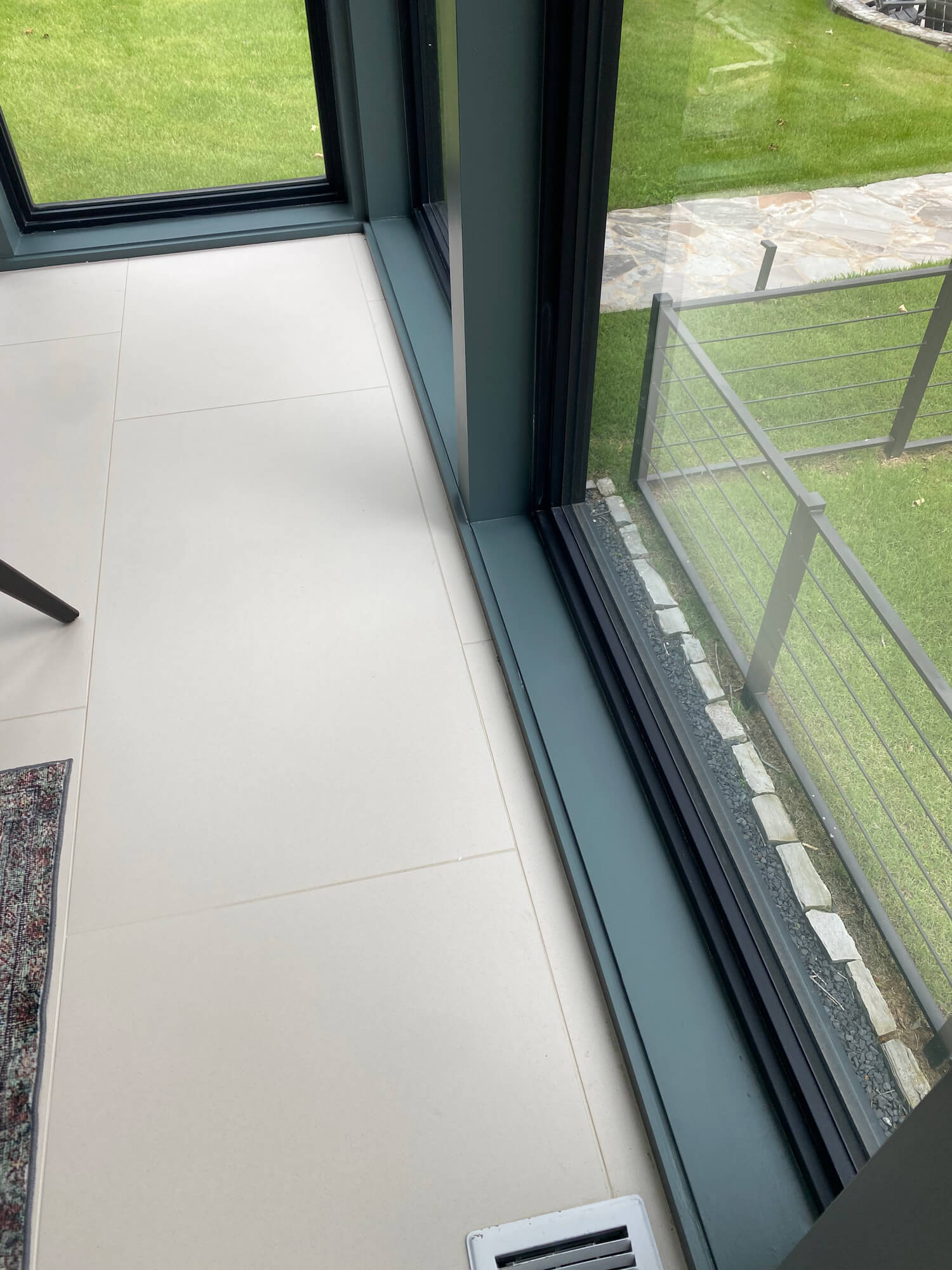 Texas Pro Painters: Modern interior space with light-colored tile flooring, large windows with dark frames, and a view of a green lawn and outdoor railing, highlighting clean lines and paintwork.