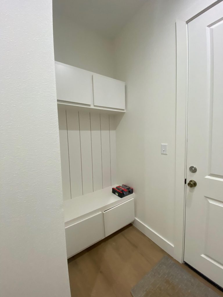 exas Pro Painters: Clean, modern mudroom or entryway with newly painted white built-in cabinetry, light wood-look flooring, and a white door, showcasing fresh interior painting.