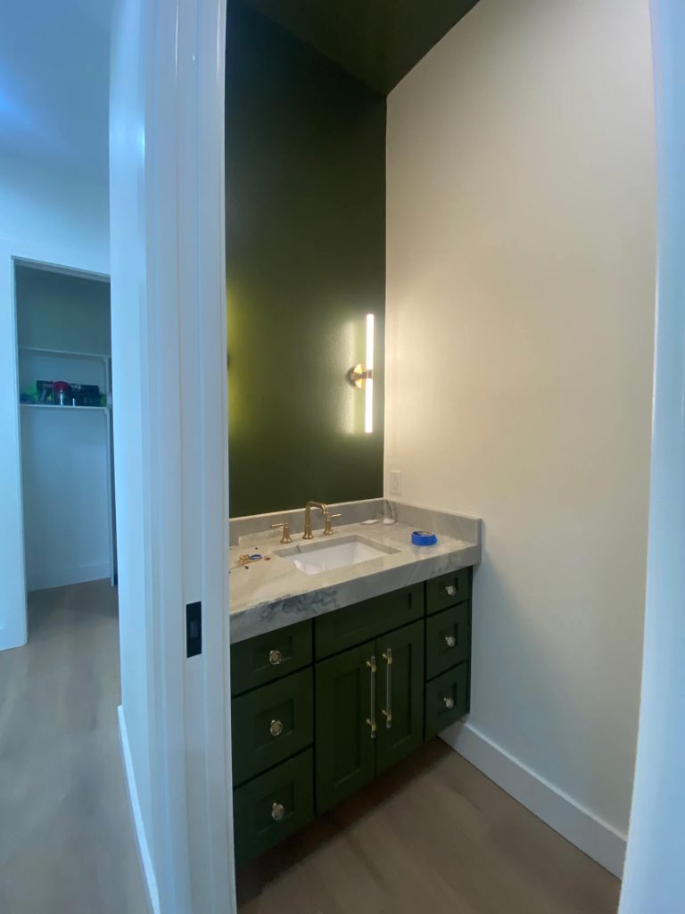 Texas Pro Painters: Stylish powder room with a dark green accent wall and matching vanity, white marble countertop, gold fixtures, and bright white walls, demonstrating bold interior painting.
