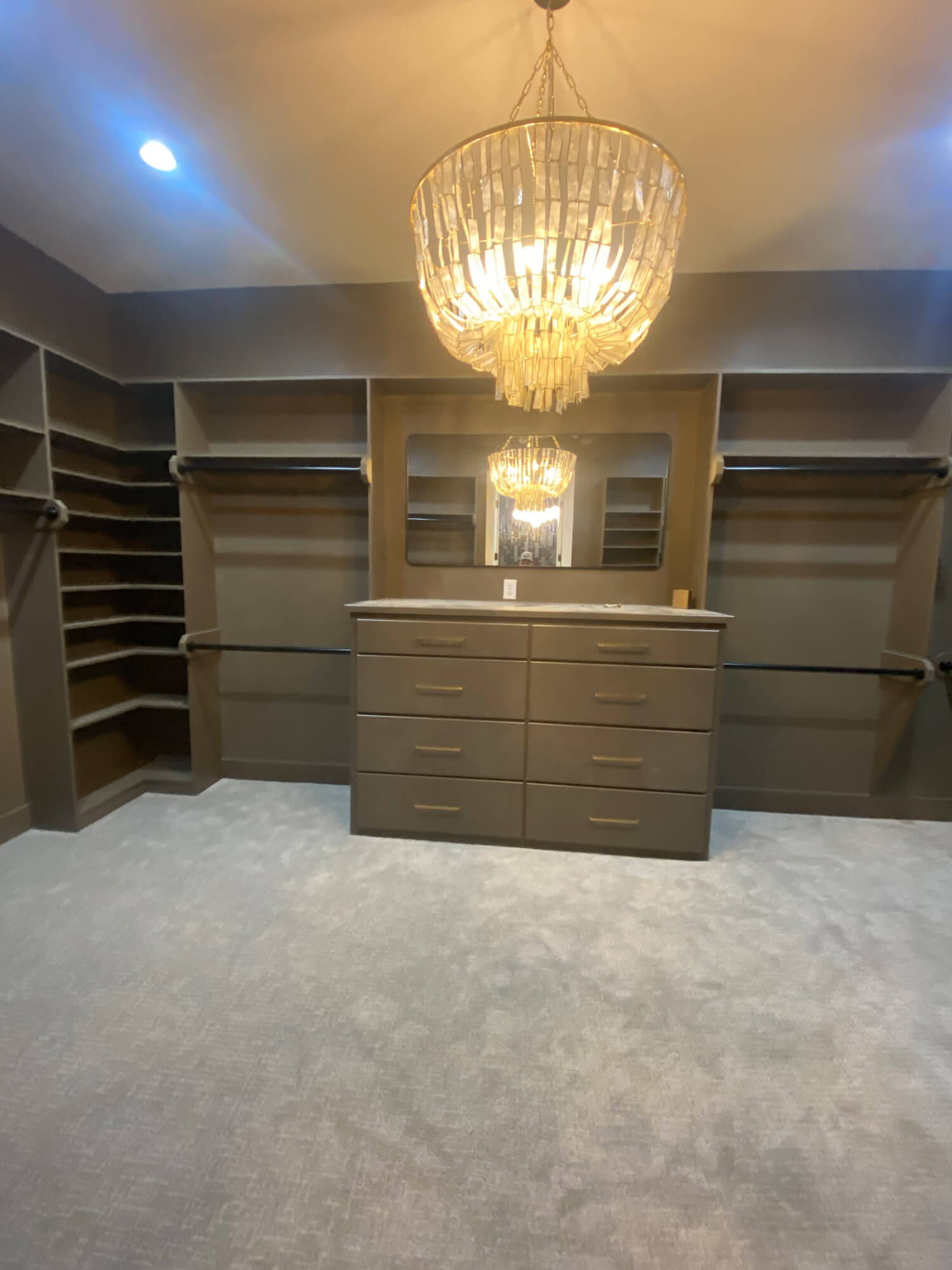 Texas Pro Painters: Custom walk-in closet featuring built-in shelving, dark grey painted walls and cabinetry, light grey carpet, and an ornate crystal chandelier, showcasing specialized interior painting.