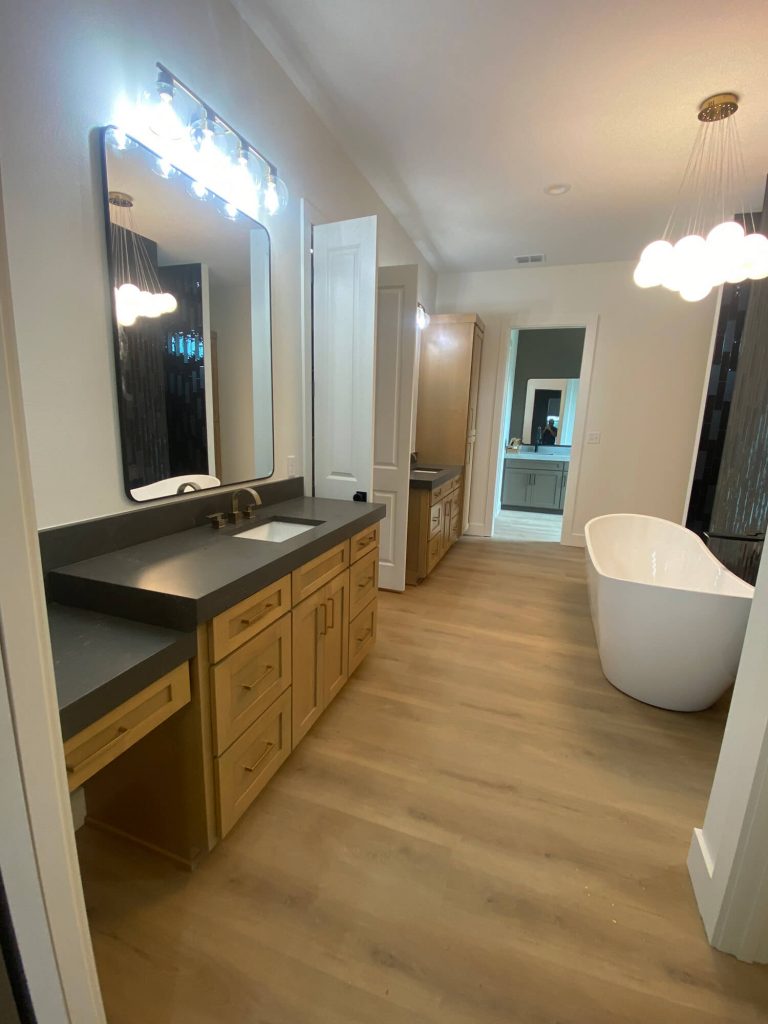 Texas Pro Painters: Luxurious modern bathroom featuring light wood vanities with dark countertops, a large free-standing tub, wood-look flooring, and unique cloud-shaped light fixtures, ideal for high-end interior painting.