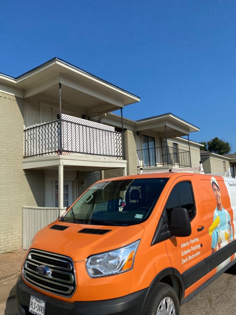 Texas Pro Painters' orange work van with branding, parked in front of a residential building with balconies, under a clear blue sky.