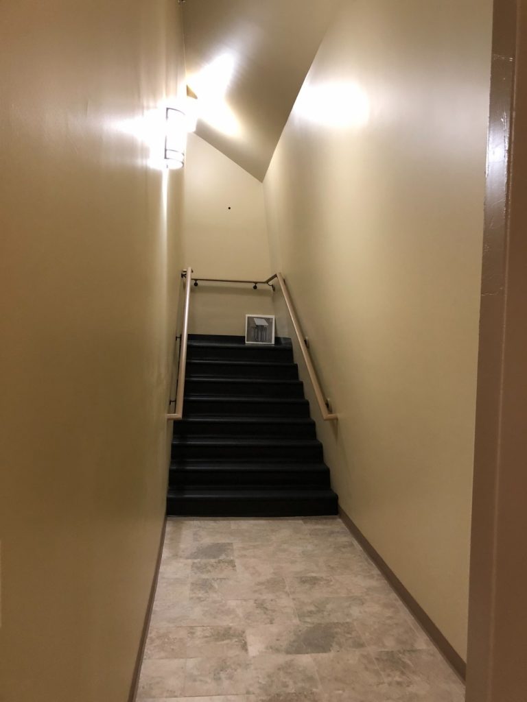 Interior staircase with light beige walls, black steps, light-colored handrails,