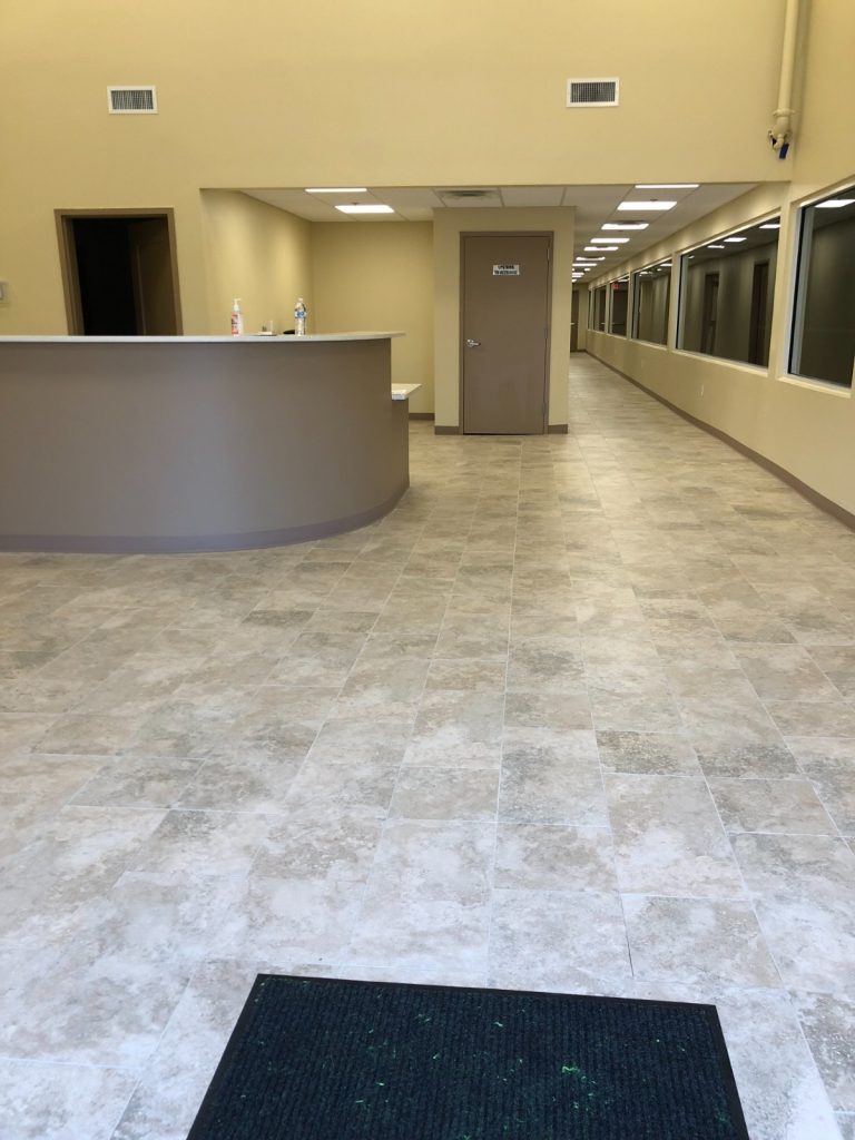 Spacious commercial reception area with a curved counter, light yellow walls, tiled flooring, and a long hallway extending into the background.