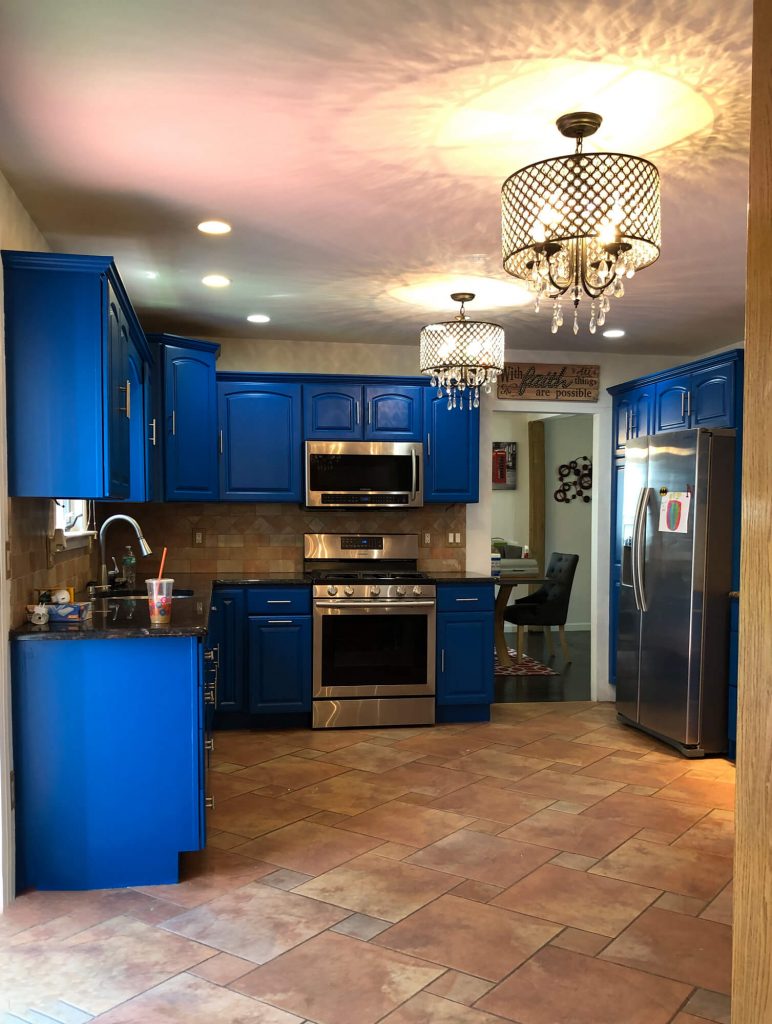 Texas Pro Painters: Vibrant kitchen with newly painted royal blue cabinets, stainless steel appliances, tiled backsplash, terracotta floor tiles, and elegant chandeliers, perfect for cabinet painting services.