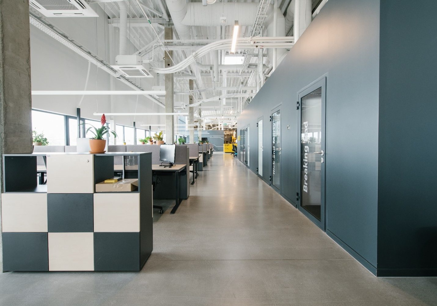 Texas Pro Painters: Contemporary open-plan office interior with exposed ceilings, long hallway of dark grey walls and glass doors, and rows of workstations.